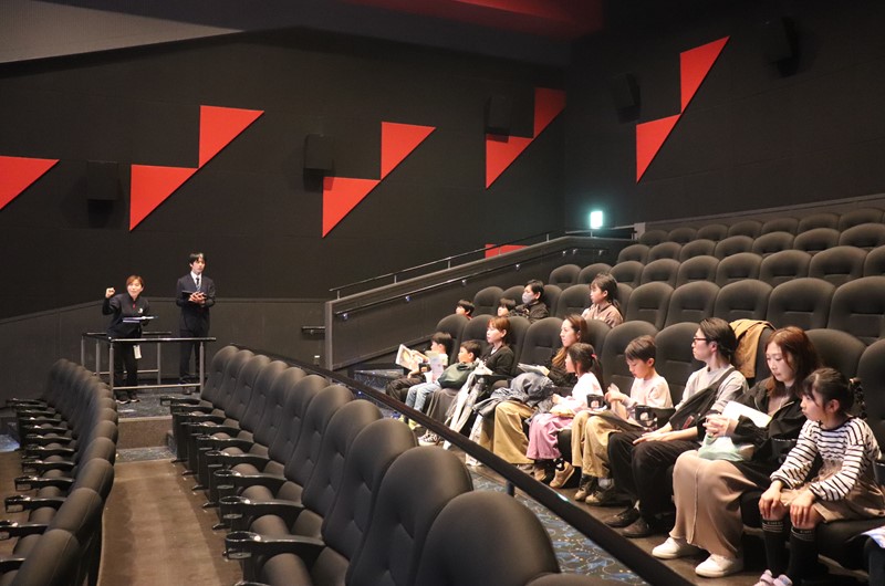誰もいない静かなスクリーンに、ツアーの案内が大きく投影され、貸切の座席で巨大な映像を見上げる子どもたちは、これから始まる未知の体験に早くも期待に胸を膨らませている様子。